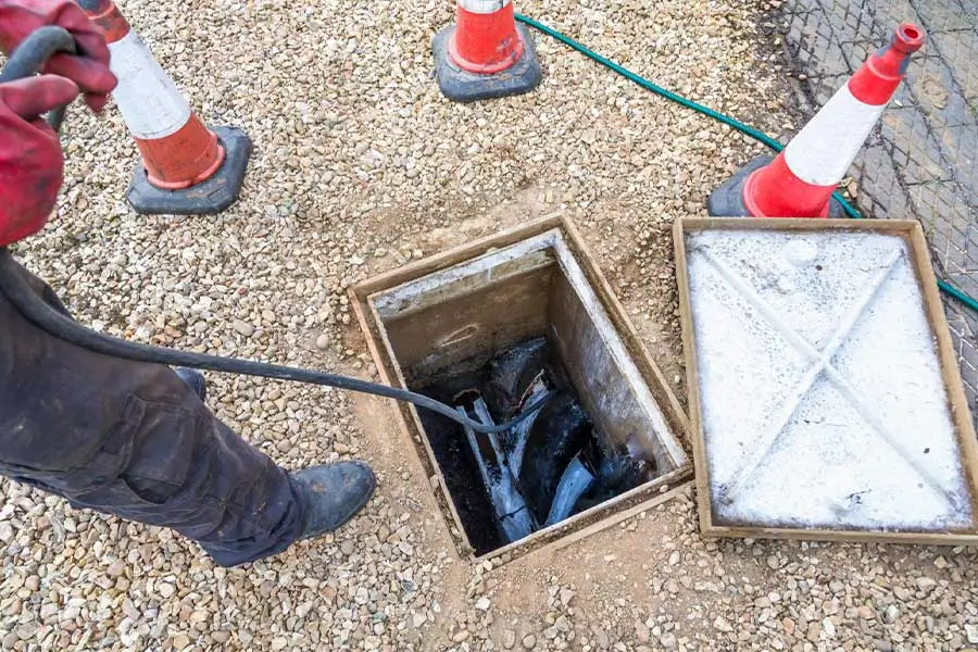Worker using a drain snake to clear an outdoor sewer line.